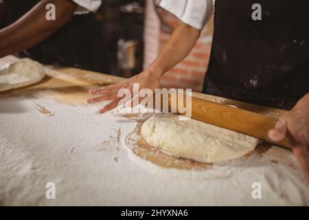 Midsection of asian mid adult female baker rolling dough on table in bakery Stock Photo