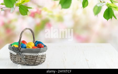 Easter eggs in a basket on white wooden table on blurred floral bakground. Copy space Stock Photo