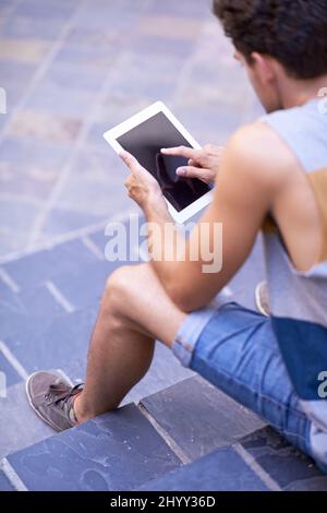 His status is always online. Over the shoulder shot of a young man sitting on steps using a tablet. Stock Photo