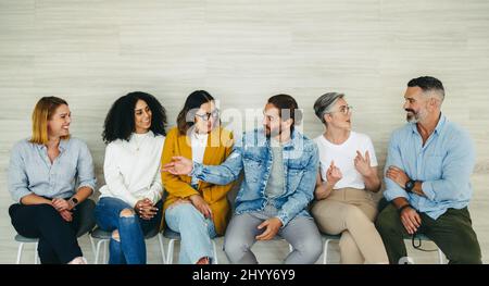 Happy businesspeople talking to each other while sitting in line for an interview. Group of successful job applicants getting to know each other in a Stock Photo