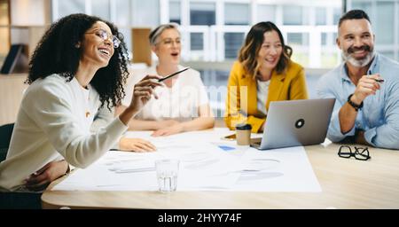 Happy design professionals smiling cheerfully during a meeting in a modern office. Group of innovative businesspeople sharing creative ideas while wor Stock Photo