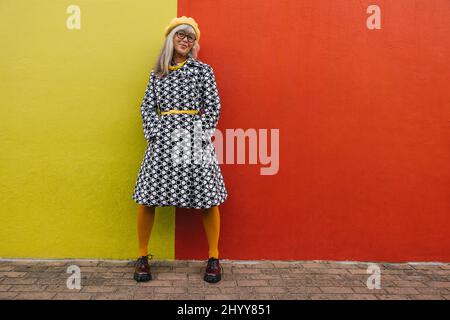 Cheerful mature woman smiling at the camera while standing against a colourful background. Happy elderly woman feeling confident and youthful while we Stock Photo