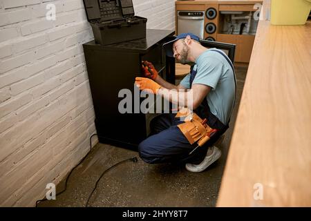 Bearded young man repairing fridge in kitchen Stock Photo