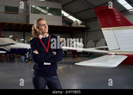 Young pilot posing smiling in the hangar surrounded by airplanes. Stock Photo
