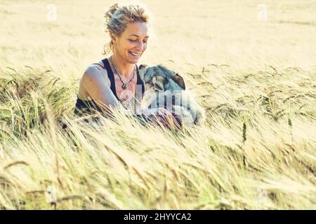 portrait of a young mature caucasian woman with her wolf dog outdoor in a cereal farmland landscape. Lifestyle concept. Stock Photo