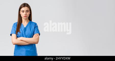 Healthcare workers, prevent virus, insurance and medicine concept. Serious and confident female nurse in blue scrubs, intern or physician cross arms Stock Photo