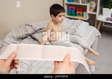 ECG film in the hands of a pediatrician cardiologist against the background of a boy of 4 years. Heart disease in children Stock Photo