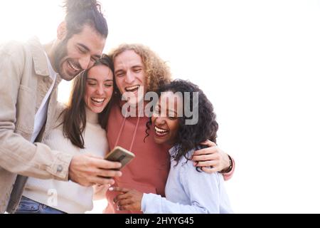 Four cheerful friends watching smartphone outdoors. People using digital device and sharing in social media togethers. Stock Photo