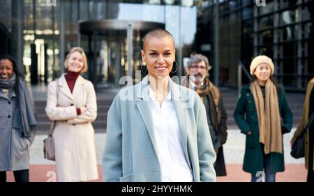 Empowered woman leads a team. Group of smiling business people outdoor in a corporate building. Stock Photo