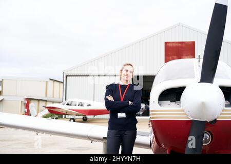 Young female pilot posing smiling next to her plane. Stock Photo
