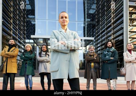 The woman director of the company poses with her team in front of the corporate building. Business people follow the leader to success and female Stock Photo
