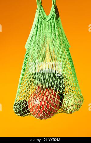 Vertical close up of fresh vegetables in eco net bag against vibrant orange background, conscious consumption Stock Photo