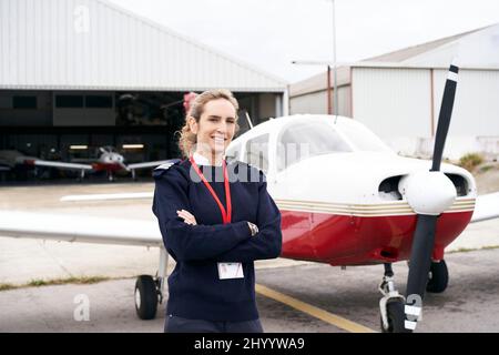 Young female pilot posing smiling in front of her plane. Stock Photo