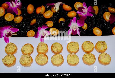 Curried chicken salad in cocktail cup hors d'oeuvre on tray decorated with blackberries, kumquats and purple orchids. Stock Photo