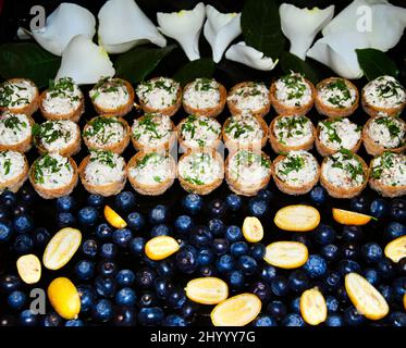 Chicken salad with tarragon in small cocktail cups on tray decorated with blueberries, kumquats and white rose petals Stock Photo