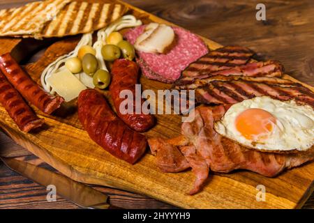 Different kinds of grilled sausages with egg. A selection of grilled gourmet meats on a rustic timber board. Grilled sausages with homemade bread. Stock Photo