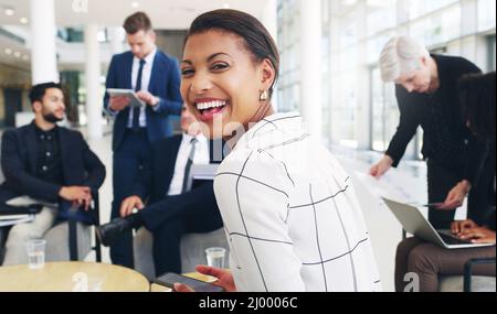 I love my colleagues. Cropped portrait of an attractive young businesswoman sitting and smiling while her colleagues work behind her in the office. Stock Photo