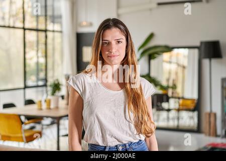 Confident beautiful blond caucasian woman with serious face standing at home looking at camera. Female entrepreneur lady posing alone, head shot close Stock Photo
