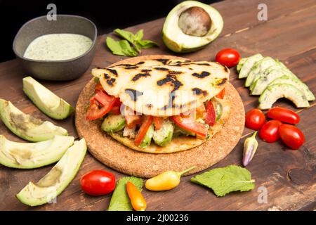 Arepas - Traditional Colombian Food originally from Latin America arranged on a old rustic wooden table mixed with meat, vegetable and  avocado Stock Photo