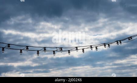 Group of light bulbs hanging with a stormy sky with clouds in the background. Stock Photo