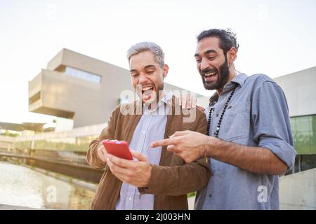 Portrait of a surprised gay couple watching something in their cell phone.  Stock Photo