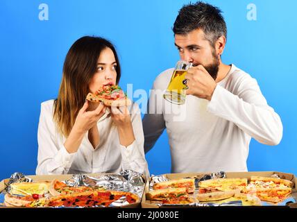 Loving couple in casual clothes eating pizza. Man drinking beer, woman eat slice pizza. Fast food. Stock Photo