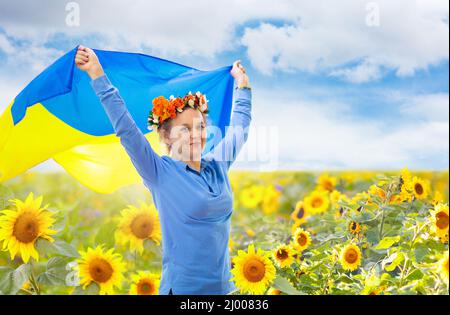 Pray for Ukraine. Woman with Ukrainian flag in sunflower field. Happy female waving national flag praying for peace. Stock Photo