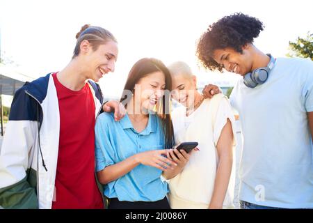 Group o friends watching the smart phone outdoor. Young smiling people sharing with mobile cell outdoors. Stock Photo