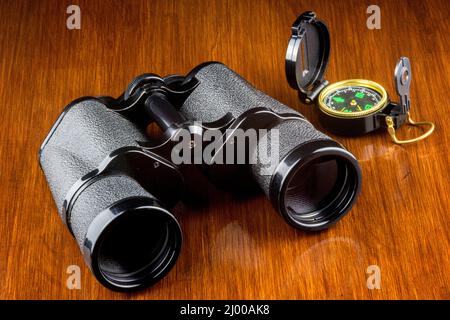 Binoculars and compass on a varnished wooden surface Stock Photo