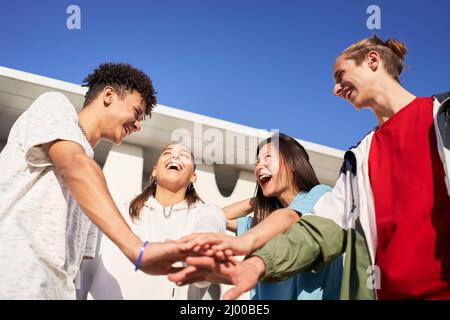 Happy young friends stacking hands. Diverse group of people celebrating and having fun together. Stock Photo