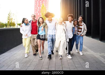 Group of young smiling people having fun outdoors. Happy students walking together and hugging on the campus college. Stock Photo
