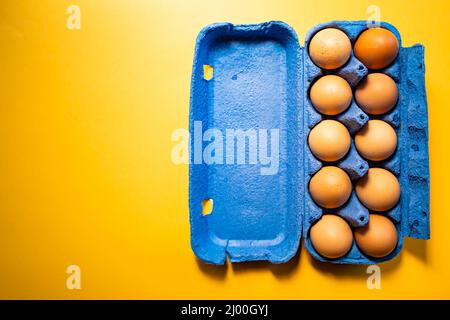 Blue eggs container with ten eggs, on yellow background. Copy space Stock Photo