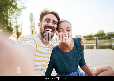 Mobile Phone selfie of a young adult caucasian couple looking camera. Happy boyfriend and smiling girlfriend having fun together Stock Photo