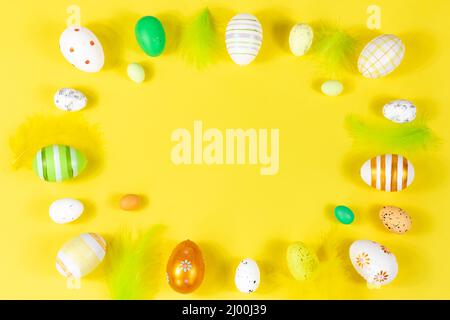 Easter frame with eggs and feathers on a yellow background. View from above. Card with copy space for text. Stock Photo