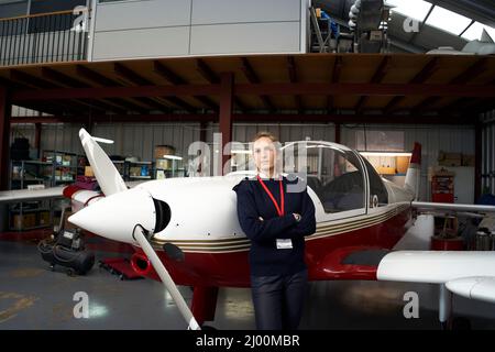 Young female pilot posing in front of her plane inside the hangar. Stock Photo