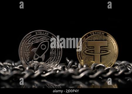 Stellar Lumens XLM And Tether USDT Cryptocurrency physical coins placed on silver chain in the black  background. Stock Photo