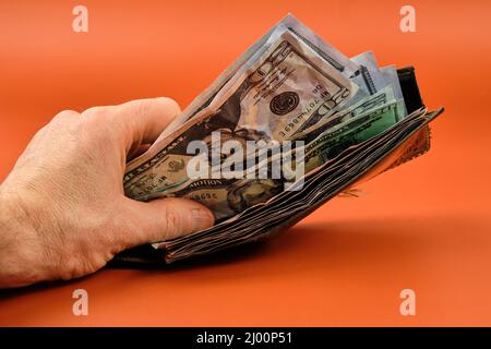 Hand showing a wallet full of bills on an orange background. Stock Photo