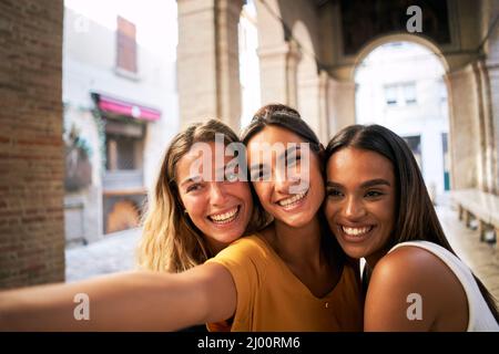 three happy female friends having fun together and taking smiling selfie Stock Photo