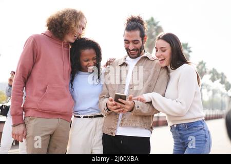 Group of happy friends using phone outdoors while walking al laughing. Stock Photo