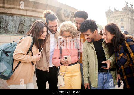 Group of cheerful friends watching smartphone outdoors. People using digital device and sharing in social media togethers. Stock Photo
