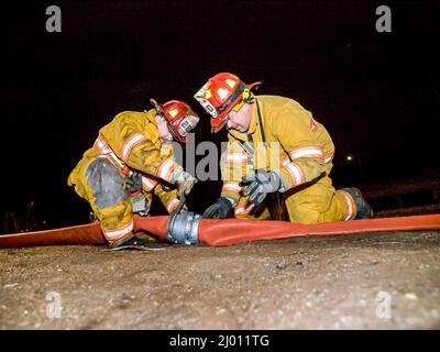 Two Firefighters in action at night with hose coupling Stock Photo