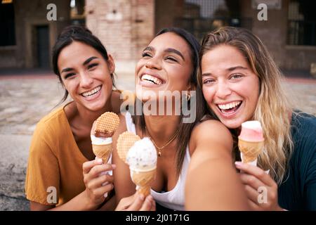 Three young smiling hipster women in summer clothes eating ice cream. Girls taking selfie self portrait photos on smartphone.Models posing in the Stock Photo