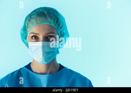 Female Surgeon Wearing protective face mask and protective suit portrait on blue background . High quality photo Stock Photo