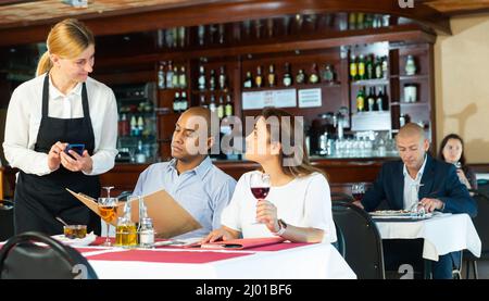 Polite waitress taking order from couple in pizza restaurant Stock Photo