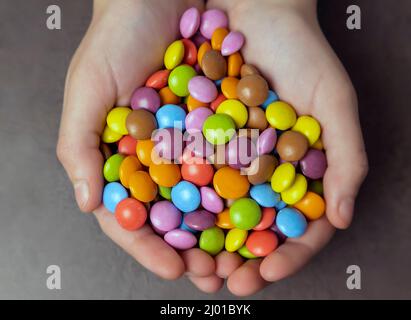 Chocolates of different colors in children's palms, children's delicacies, top view. Stock Photo