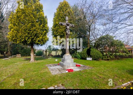 Wooden crucifix with Remembrance Day poppy wreaths in St Michael and All Angels churchyard, Pirbright village, near Woking, Surrey, south-east England Stock Photo