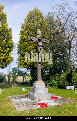 Wooden crucifix with Remembrance Day poppy wreaths in St Michael and All Angels churchyard, Pirbright village, near Woking, Surrey, south-east England Stock Photo