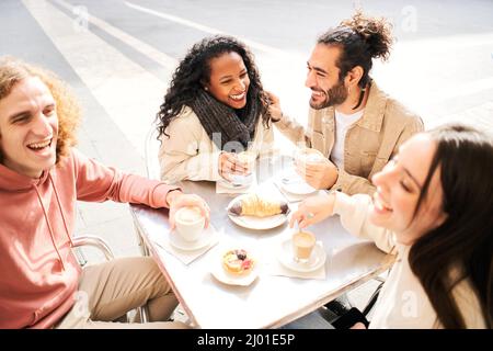 Group of young multiracial people having breakfast in an outdoor coffee shop. Students of different countries having fun together drinking coffees and Stock Photo