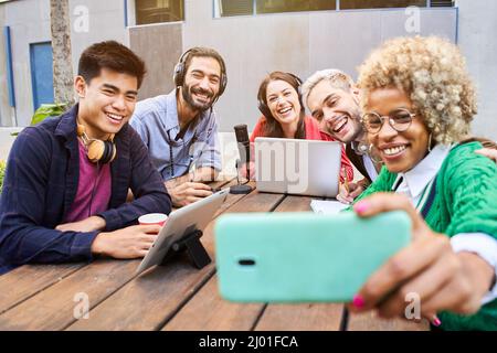 Happy friends taking selfie during gathering. Radio hosts recording podcast outdoors Stock Photo
