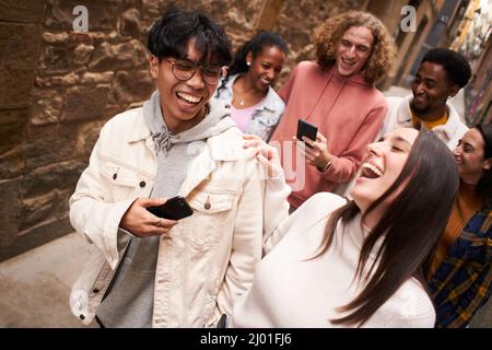 Group of happy friends using the mobile in the street. Young people in. social media take a walk. Stock Photo